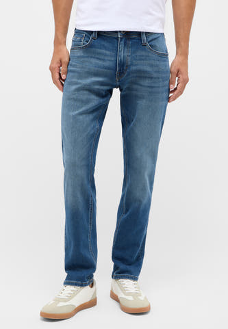 Blauwe slim jeans van MUSTANG, zichtbaar zijn de subtiele wassingen en de styling met witte sneakers.
