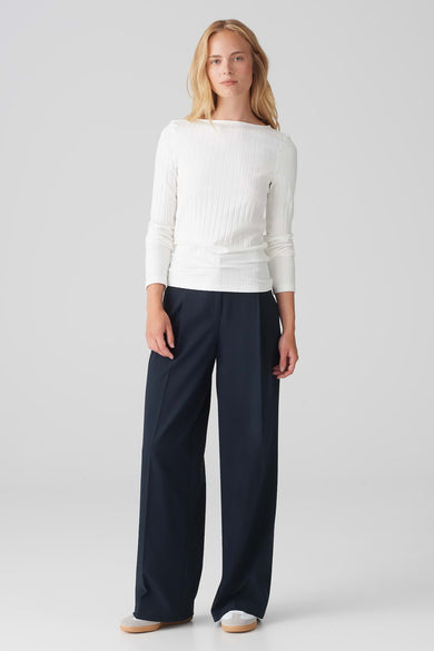 Witte trui met ronde hals van OPUS, geribbelde textuur, gecombineerd met donkerblauwe, wijde broek en crèmekleurige schoenen.