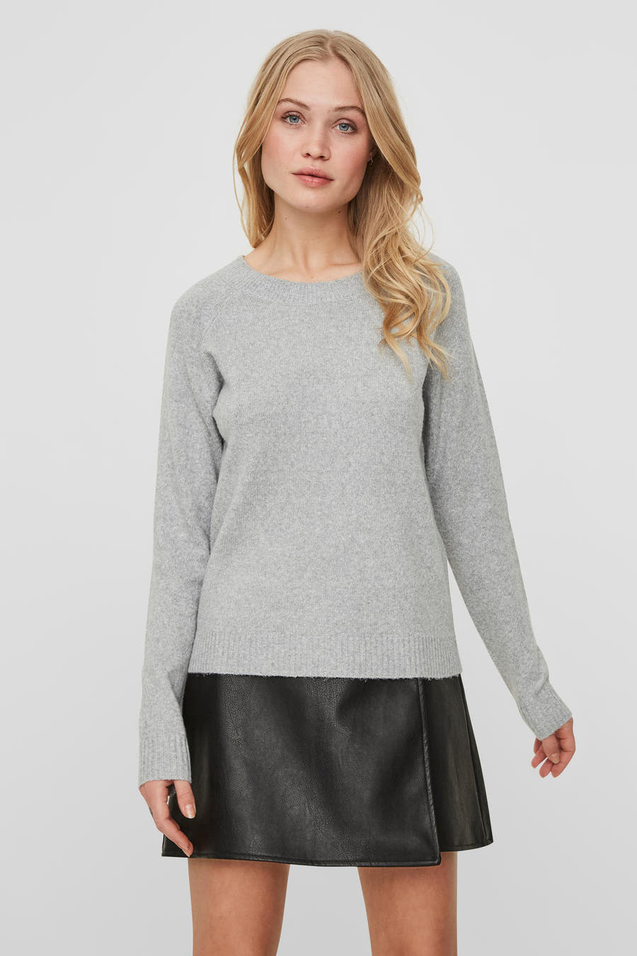 Grijze trui van VERO MODA, gedragen met een zwarte leren rok, op een witte achtergrond.
