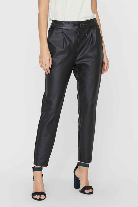Zwarte leerlook broek van VERO MODA® met paperbag taille, plooien en aantrekkoord, gedragen met witte top en donkerblauwe sandalen.
