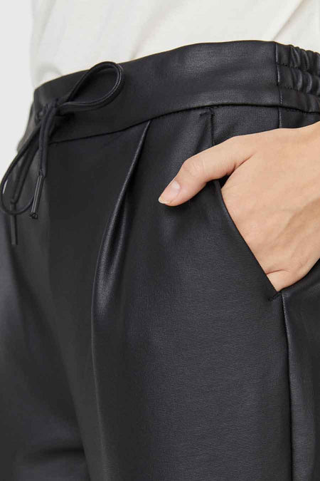 Zwarte broek van imitatieleer van VERO MODA® met tunnelkoord, elastische taille en plooien, met een hand in de zak.