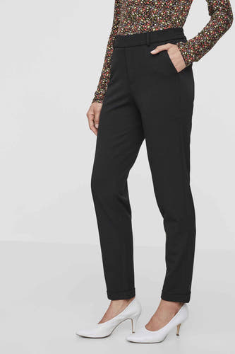 Zwarte kostuumbroek van VERO MODA, met steekzakken en omgeslagen pijpen, gecombineerd met een bloemenprint shirt en witte pumps.
