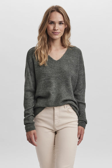 T-shirt vert de Vero MODA avec un col en V, porté avec un pantalon crème et des cheveux blonds décolorés.