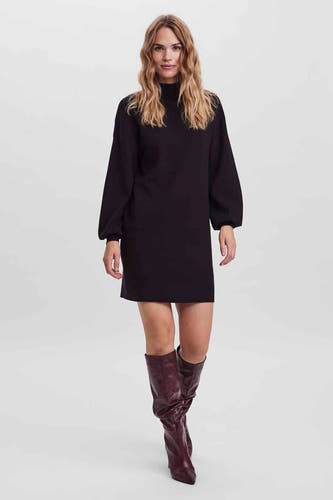 Robe noire à manches longues de VERO MODA, associée à des bottes hautes dans une composition studio.