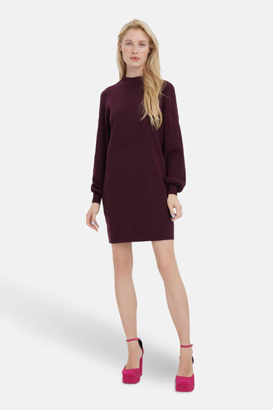 Vrouw in een bordeauxrode jurk met lange mouwen en roze platformschoenen.