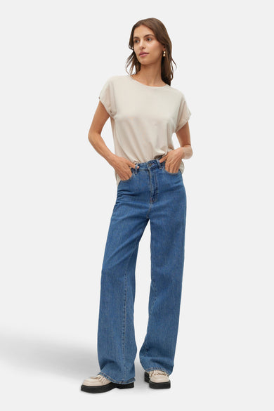 T-shirt beige à manches courtes de VERO MODA®, porté avec des jeans bleus larges et des chaussures crème à semelle épaisse.