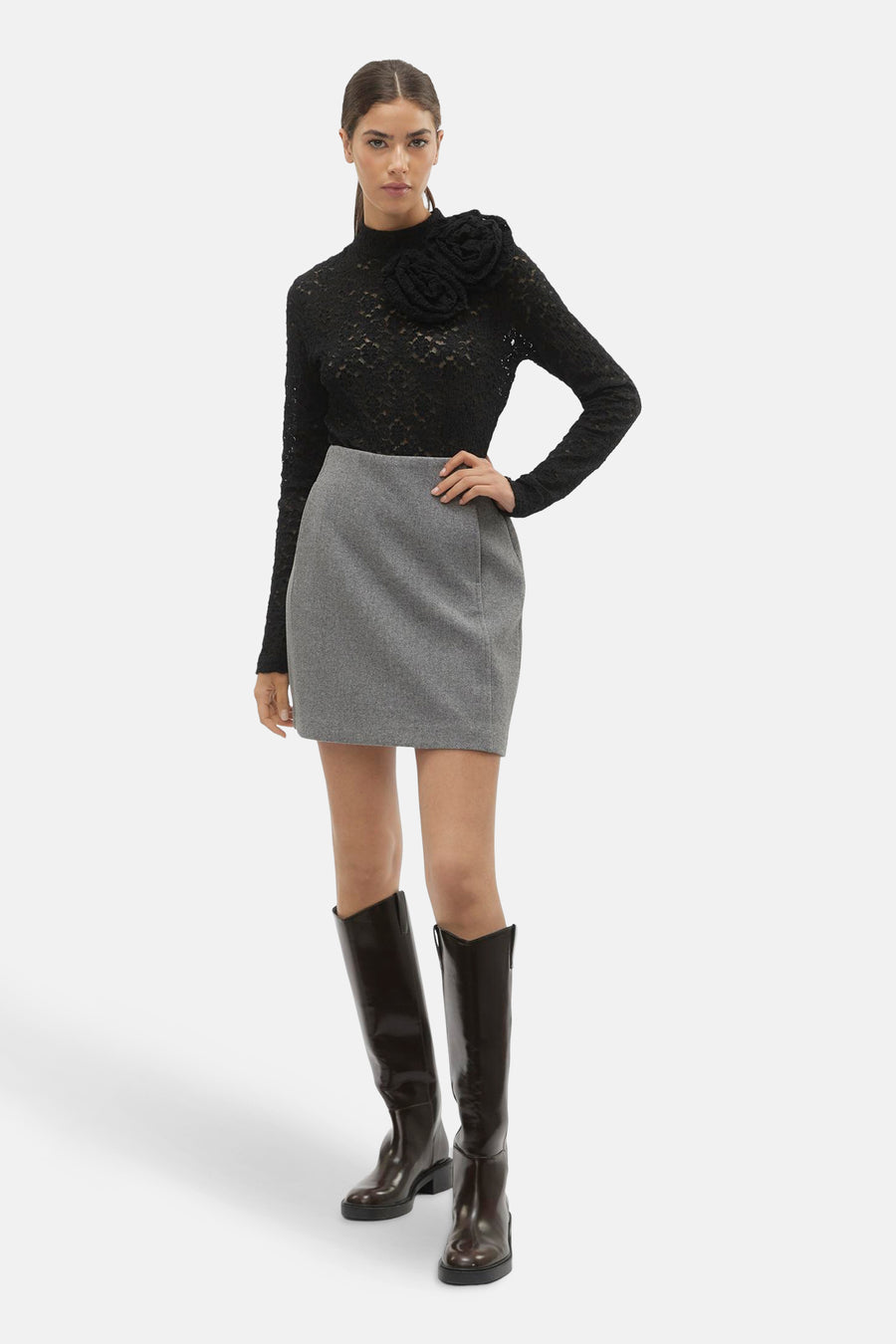 Jupe grise courte de VERO MODA, associée à une chemisier en dentelle et des bottes brunes longues.