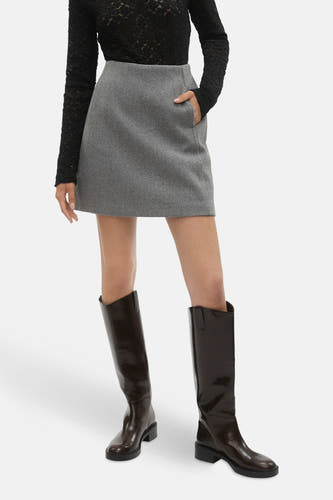 Jupe grise courte de VERO MODA®, avec poche et associée à une chemisier noire et des bottes marron.