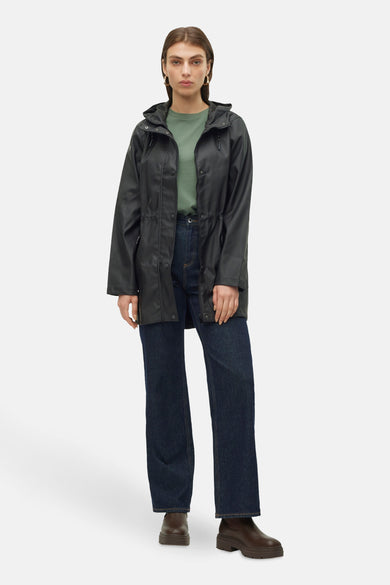 Zwarte regenjas van VERO MODA, met capuchon, koord in de taille en gecombineerd met donkere jeans en bruine laarzen.