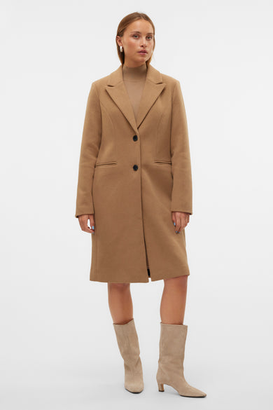 Bruine lange jas van Vero Moda met zwarte knopen, gedragen met een beige coltrui en suède laarzen.
