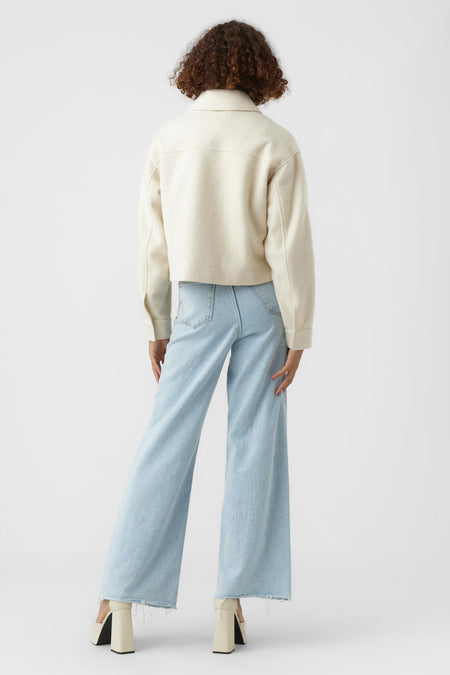 Beige korte jas van VERO MODA®, achterzijde, met opstaande kraag en zachte textuur, gedragen met lichtblauwe wijde jeans en crèmekleurige hakken
