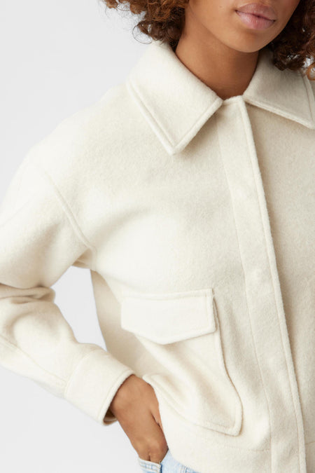 Beige korte jas van VERO MODA® met zachte textuur, opstaande kraag en borstzakje, close-up van model met hand in zak
