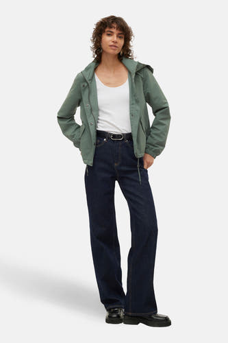 Korte groene jas van VERO MODA, met een capuchon, gedragen met een wit shirt en een donkere broek.