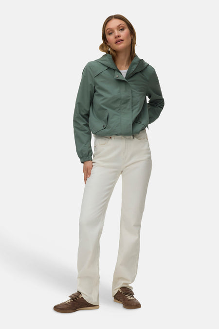 Groene korte jas van VERO MODA, met lange mouwen, capuchon en witte broek en bruine schoenen.
