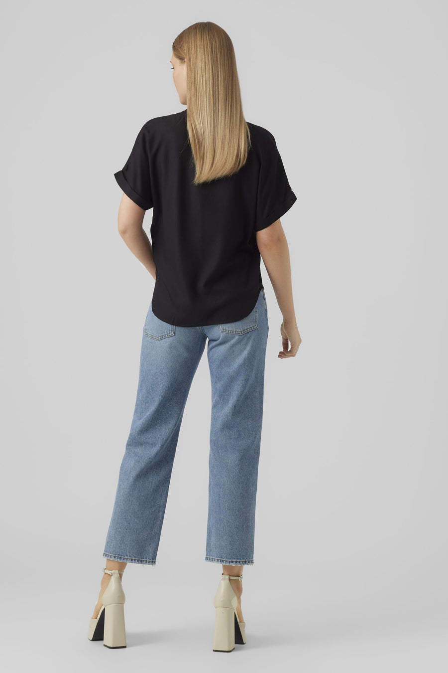 Chemisier noir à manches courtes de VERO MODA, vu de dos, combiné avec un jean bleu et des talons beiges.