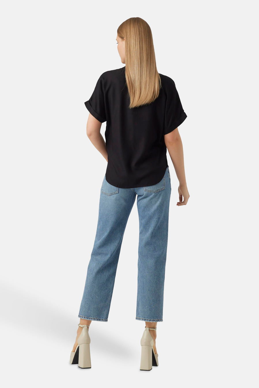 Zwarte blouse met korte mouwen van VERO MODA®, gezien van achteren, gecombineerd met blauwe jeans en beige hakken.
