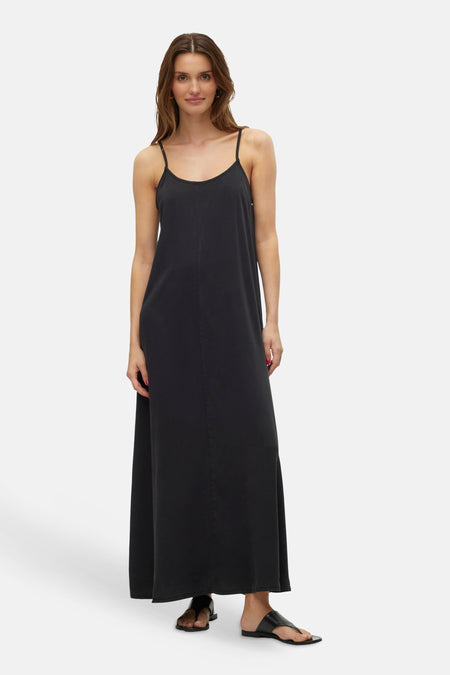 Zwarte mouwloze jurk van VERO MODA®, maxi-lengte met spaghettibandjes en zwarte sandalen.
