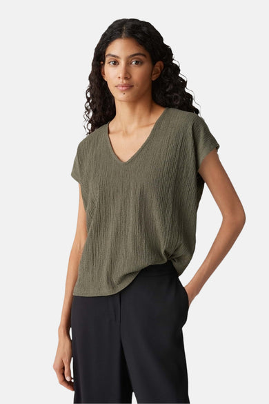 Blouse kaki à manches courtes d'OPUS, avec un col V et une texture plissée, associée à un pantalon noir.