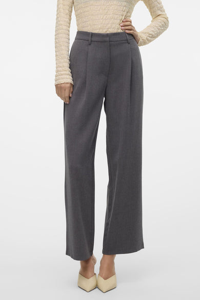 Pantalon gris de VERO MODA, pinces tombantes, taille haute, associé à une chemise blanche et des chaussures pointues.