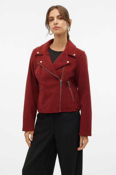 Bruine korte jas van VERO MODA, met asymmetrische rits en zilverkleurige details, gecombineerd met zwarte pantalon en gouden oorbellen.
