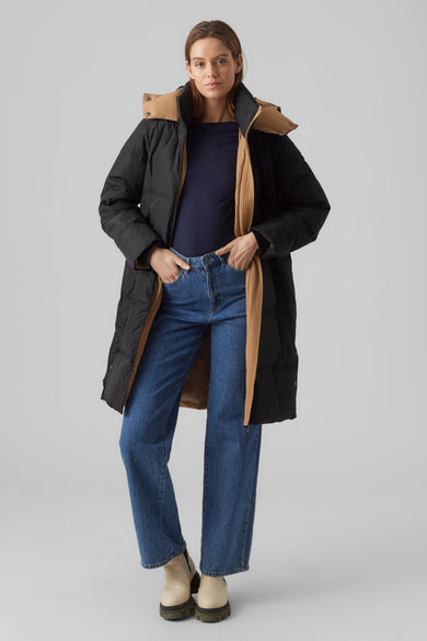 Zwarte lange jas van Vero Moda met een bruine kraag, gedragen met jeans en laarzen.
