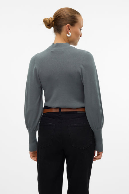 Veste verte VERO MODA®, vue de derrière, avec des manches longues et un jeans noir avec une ceinture marron.