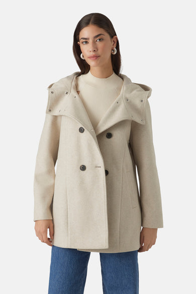 Beige korte jas van Vero Moda met een capuchon en dubbele knoopsluiting, gedragen met een gebreide trui en jeans.
