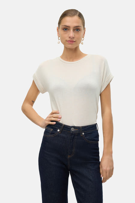 Beige T-shirt met korte mouwen van VERO MODA®, gecombineerd met donkere jeans en parel oorbellen.
