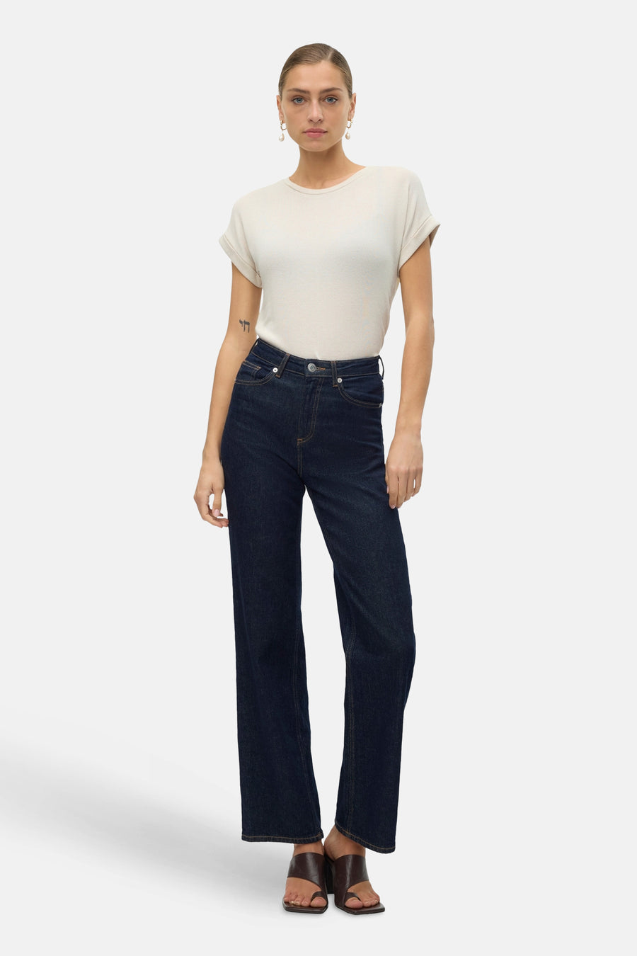 Beige T-shirt met korte mouwen van VERO MODA, gedragen met donkerblauwe jeans en bruine muiltjes.