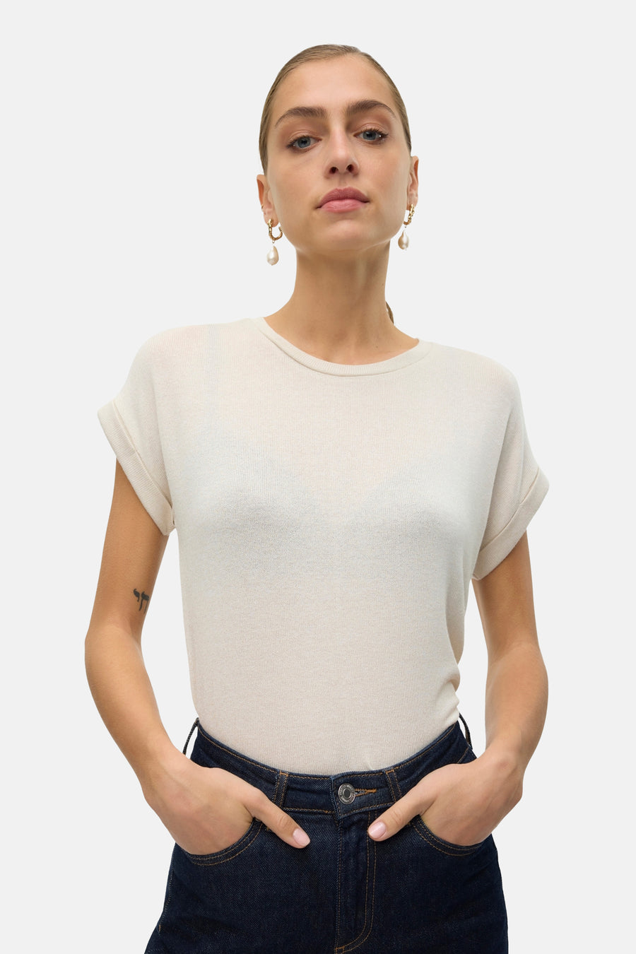Beige T-shirt met korte mouwen van VERO MODA®, met opgerolde mouwen en donkere jeans met de handen in de zakken.