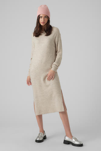Beige kleedje met lange mouwen van VERO MODA, met een split aan de zijkant en gedragen met een roze muts en zilverkleurige schoenen.
