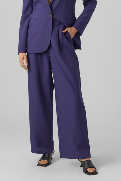 Blauwe broek van Vero Moda, met wijde pijpen en een hand in de zak, gecombineerd met zwarte muiltjes.
