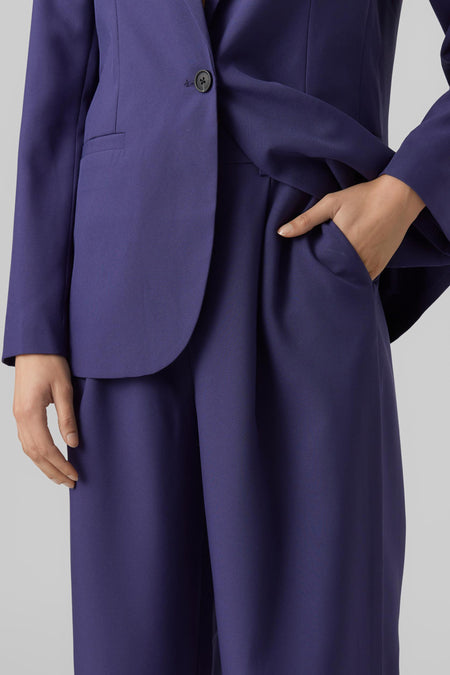 Blauwe broek van VERO MODA, met een hand in de zak en een bijpassende blazer.
