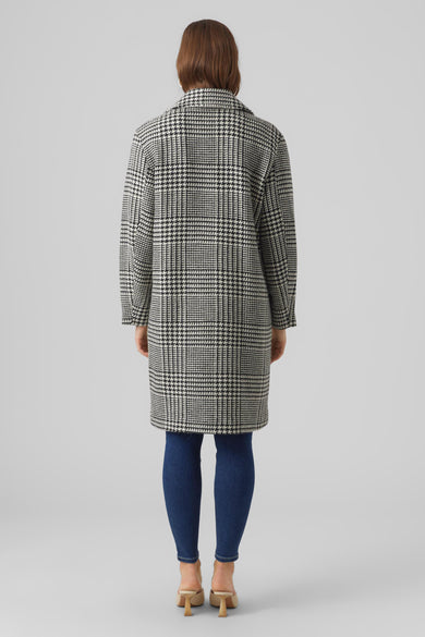 Manteau long noir de VERO MODA, avec un motif pied-de-poule, associé à des jeans bleus et des mocassins beige.