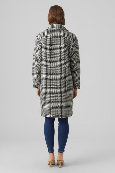Manteau long noir de VERO MODA, avec un motif pied-de-poule, associé à des jeans bleus et des mocassins beige.
