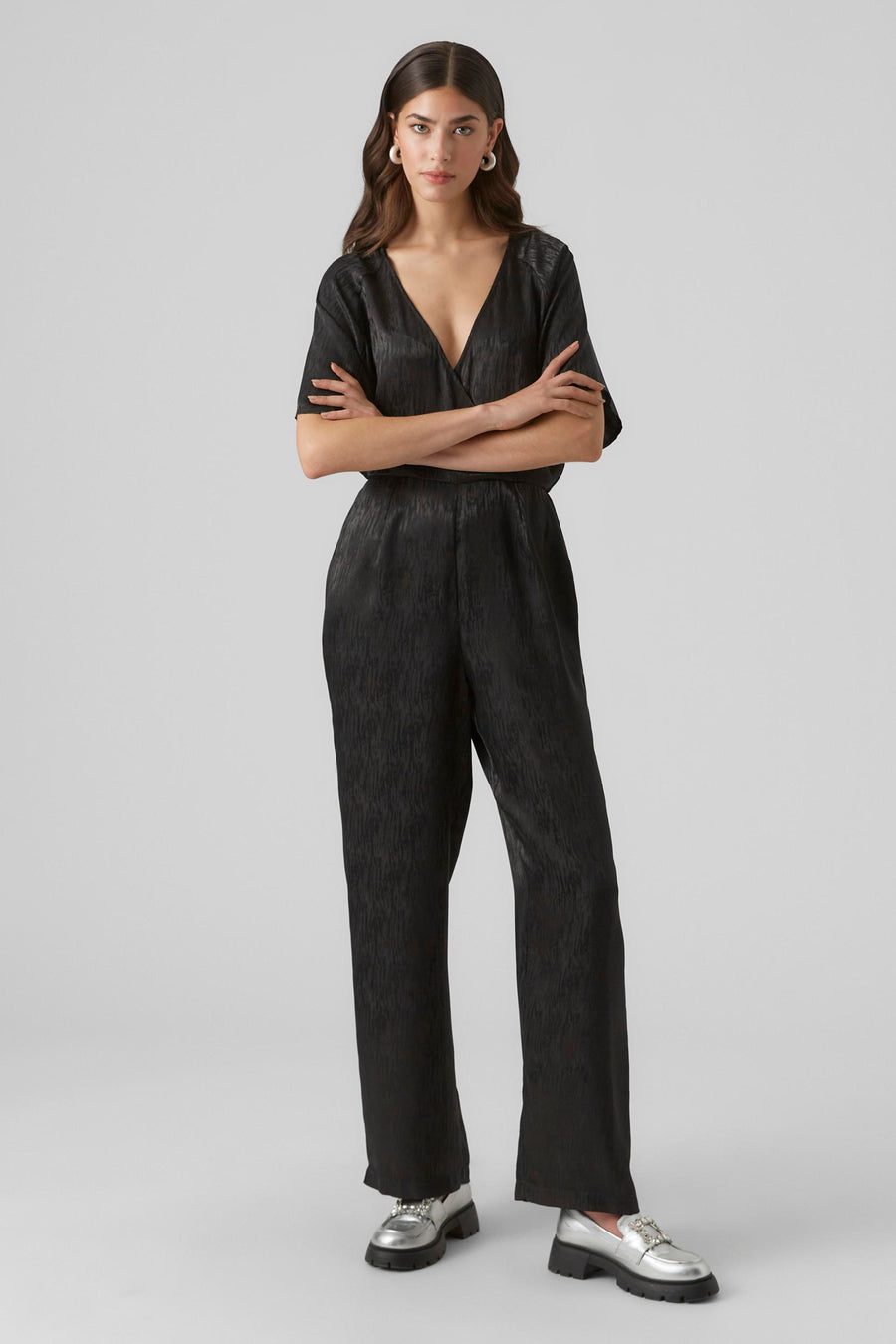 Combinaison noire de VERO MODA, avec des manches courtes et un col V, portée avec des chaussures argentées.