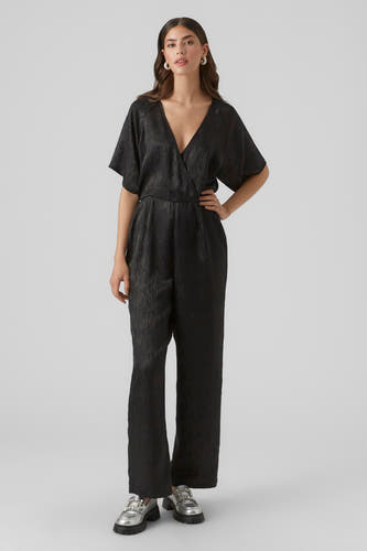 Combinaison noire de VERO MODA, avec des manches courtes, un col montant et des jambes larges, portée avec des loafers argentés ornés de strass.