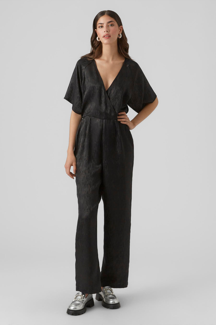 Combinaison noire de VERO MODA, avec des manches courtes, un col montant et des jambes larges, portée avec des loafers argentés ornés de strass.