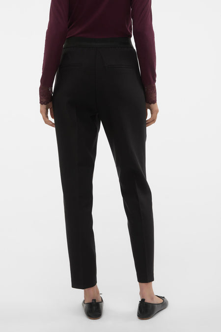 Pantalon noir de VERO MODA, avec des poches arrière et une ceinture élastique, porté avec un haut bordeaux.