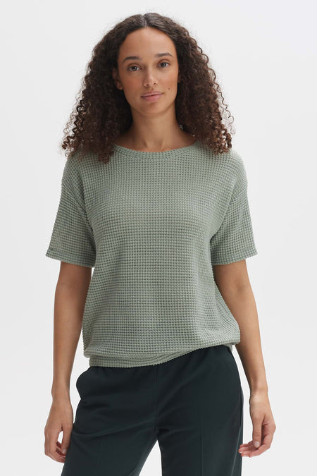 T-shirt à manches courtes vert clair d'OPUS avec un motif gaufré fin, porté par un mannequin aux cheveux bouclés.