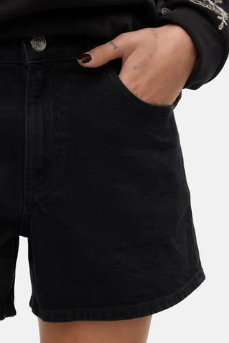 Short noir de VERO MODA, avec la main dans la poche et une subtile tatouage sur la main.