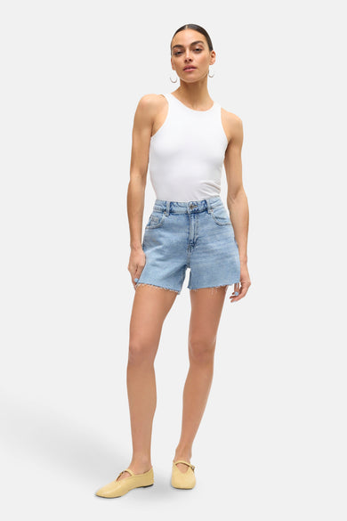 Short en denim bleu clair de VERO MODA, avec des bords froncés et porté avec un haut blanc et des chaussures plates.