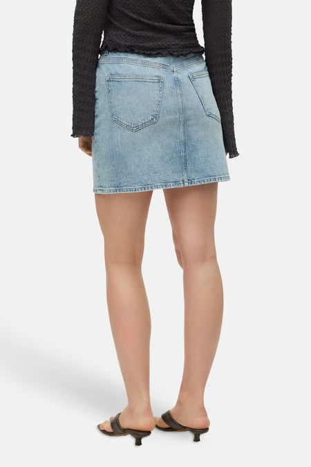 Korte rok in lichtblauw denim van VERO MODA® met twee achterzakken, van achteren gezien, gedragen met een zwarte top en hakken.