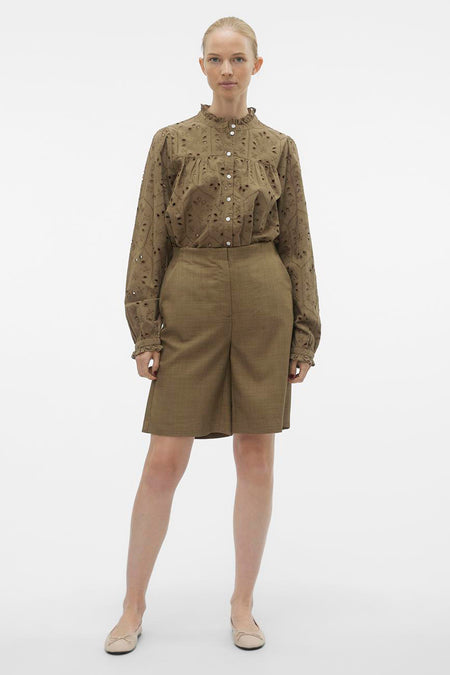 Bruine short van VERO MODA, gecombineerd met een geborduurde blouse met lange mouwen en platte schoenen.
