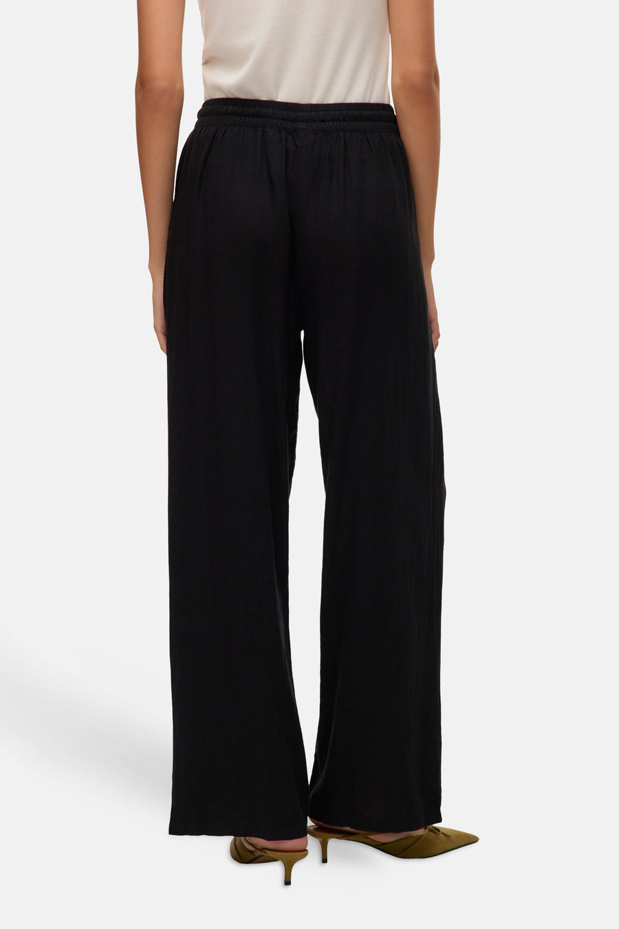 Zwarte broek van VERO MODA®, met wijde pijpen en elastische tailleband, gezien van achteren met hakken.
