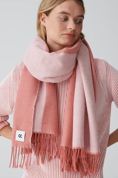 Oranje wintersjaal van OPUS, met roze baan en franjes, gedragen met een gestreepte blouse.
