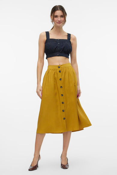 Zwarte blouse van VERO MODA, met knoopsluiting, gecombineerd met een okergele rok met knopen en hakken.