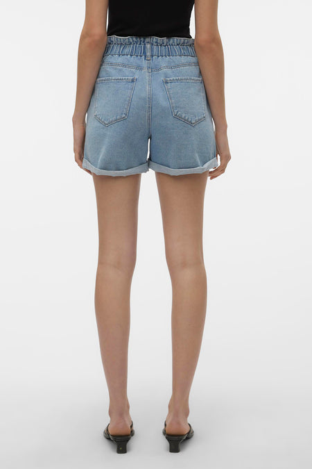Blauwe denim short van VERO MODA® met hoge elastische paperbag taille, omgeslagen pijpen en achterzakken. Van achteren gezien, gedragen met een zwarte top en muiltjes.