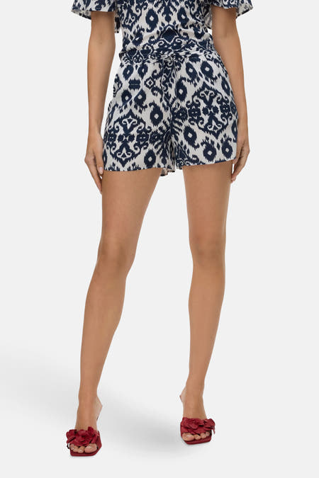 Blauwe short van VERO MODA met ikat-patroon, gestrikt in de taille en gecombineerd met rode open schoenen.
