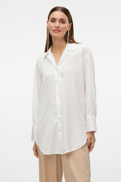 Wit overhemd met lange mouwen van VERO MODA®, met subtiel verticaal patroon en gedragen met een beige pantalon.
